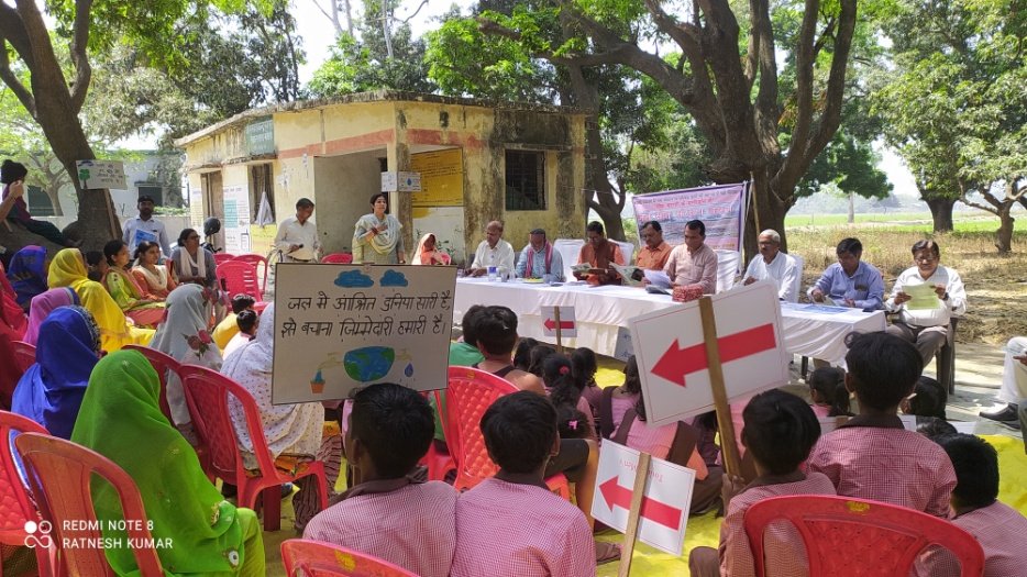 Water conservation awareness meeting with villagers and officials, with a poster reading 'the world depends on water, saving it is our responsibility'